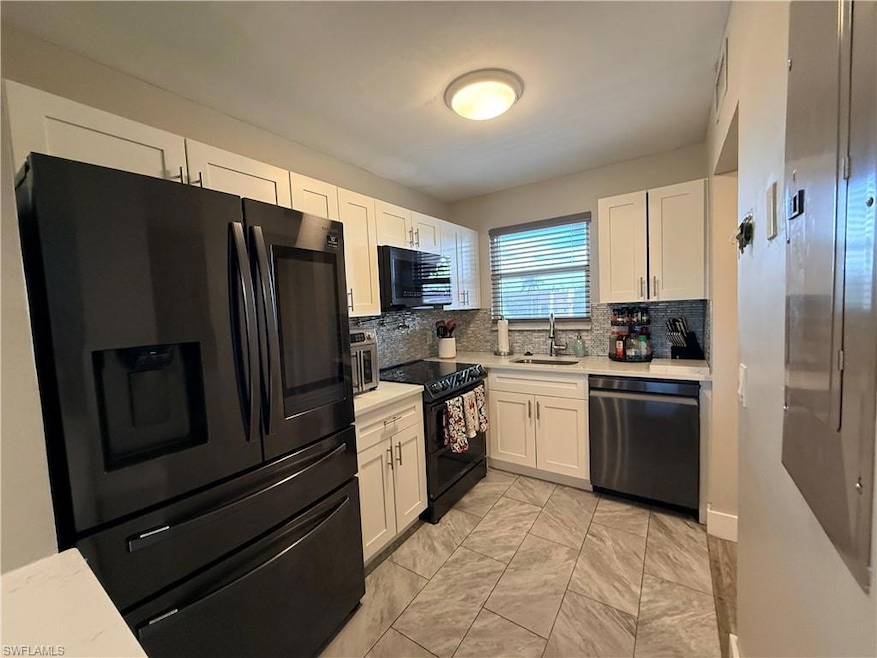 Kitchen featuring black appliances, backsplash, white cabinetry, and light stone countertops