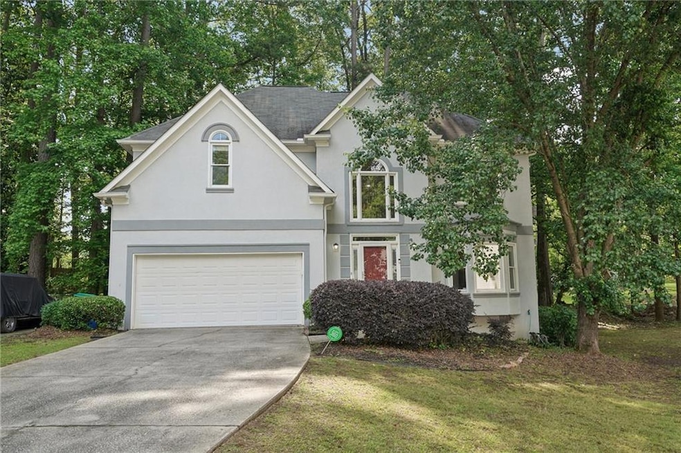 Traditional home featuring stucco siding, driveway, an attached garage, and a front lawn