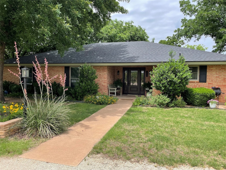Ranch-style house with a front lawn, roof with shingles, brick siding, and a porch