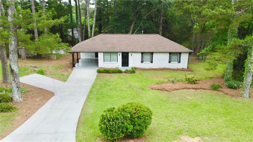 View of front of property featuring driveway, roof with shingles, a front yard, an attached carport, and stucco siding