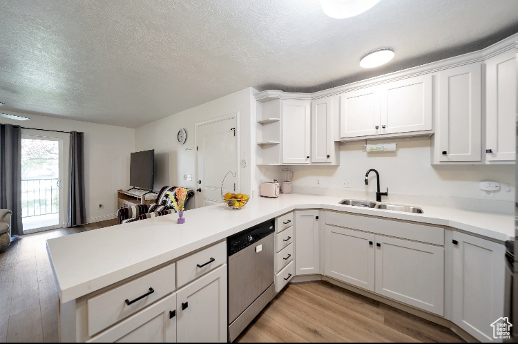 Kitchen with open floor plan, light wood finished floors, a textured ceiling, light countertops, and dishwasher