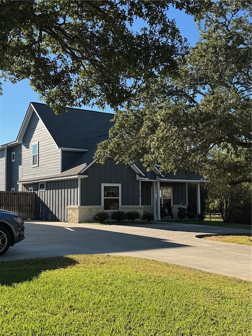 View of front of property featuring board and batten siding, roof with shingles, driveway, a porch, and stone siding