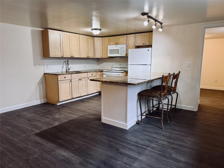 Kitchen with dark hardwood / wood-style flooring, white appliances, a breakfast bar area, and light brown cabinetry