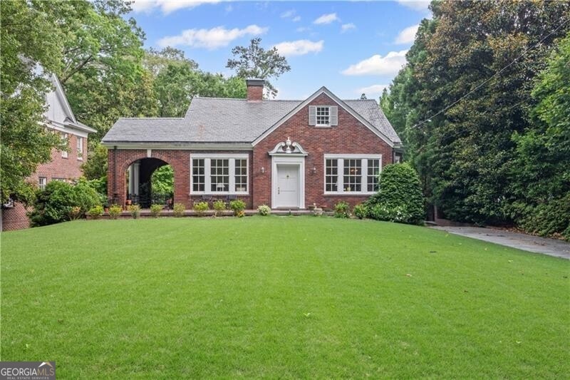 View of front facade featuring 4-sided brick, a chimney, and a lush front yard