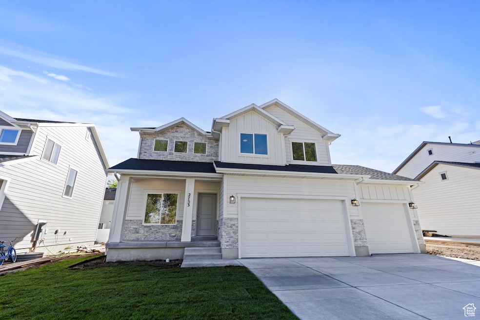 View of front of property featuring board and batten siding, stone siding, concrete driveway, and a front lawn.