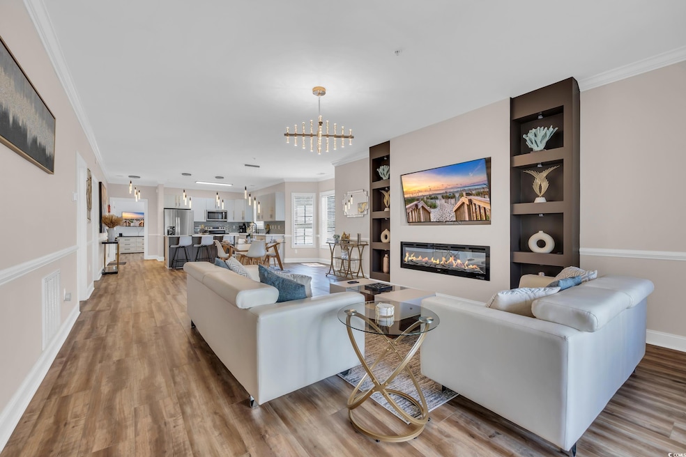 Living area featuring a glass covered fireplace, ornamental molding, light wood-style flooring, and a chandelier