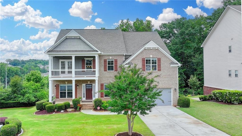 View of front facade featuring brick siding, a balcony, concrete driveway, an attached garage, and a front yard