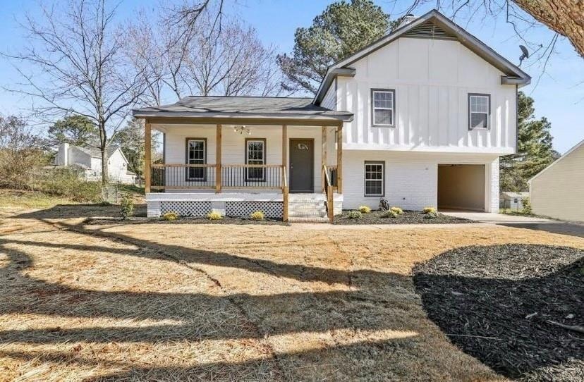 Tri-level home featuring a porch, an attached garage, board and batten siding, and brick siding