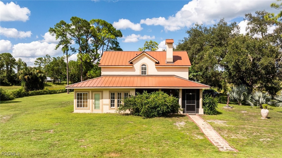 Rear view of house featuring a lawn, a chimney, a sunroom, and a metal roof