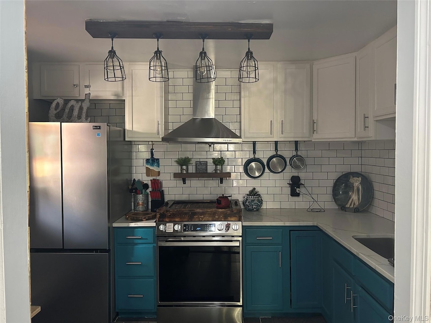 Kitchen with blue cabinets, appliances with stainless steel finishes, backsplash, and white cabinetry