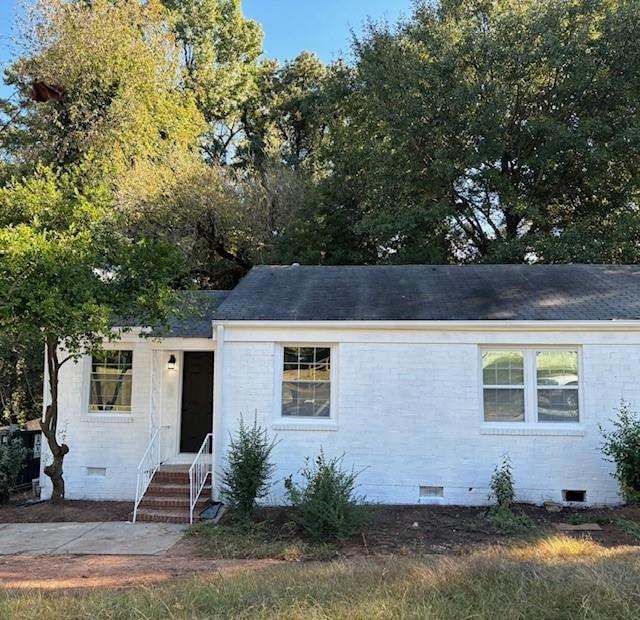 View of front of property with crawl space, brick siding, and roof with shingles