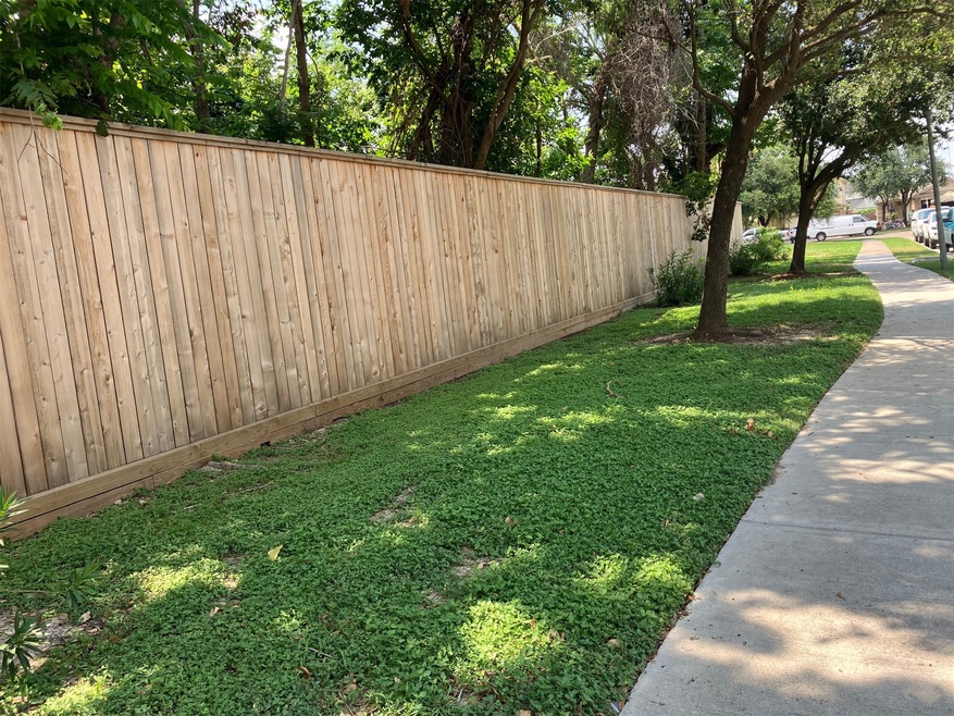 A wooden fence along a sidewalk with lush green gr