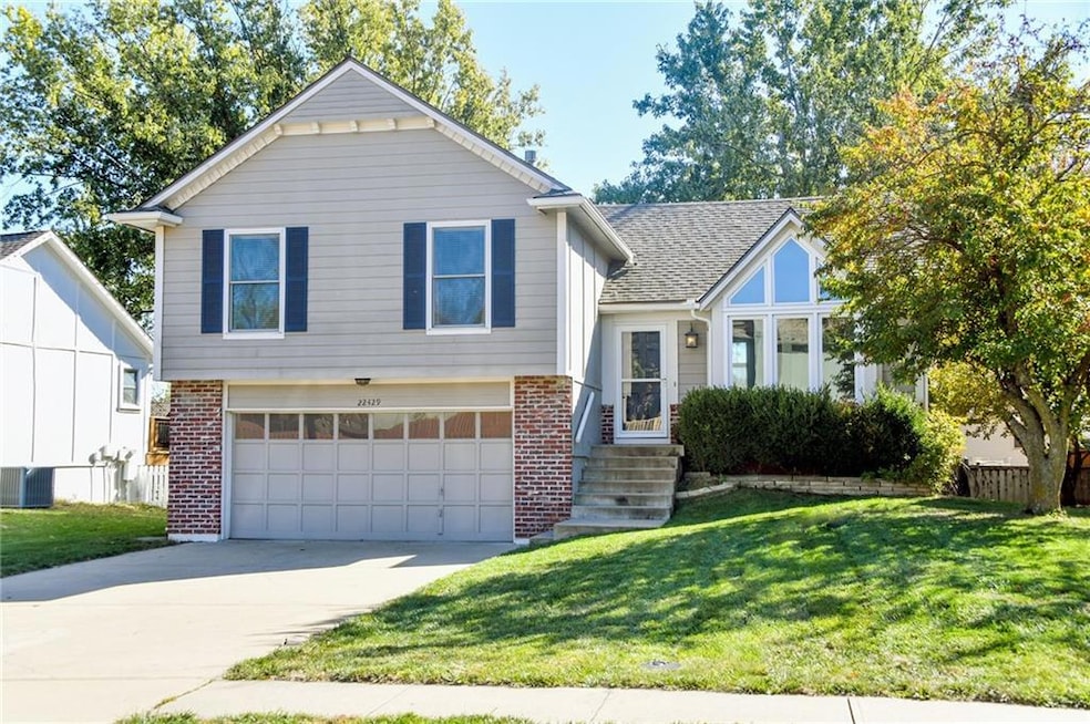 Tri-level home featuring brick siding, a garage, driveway, and a shingled roof