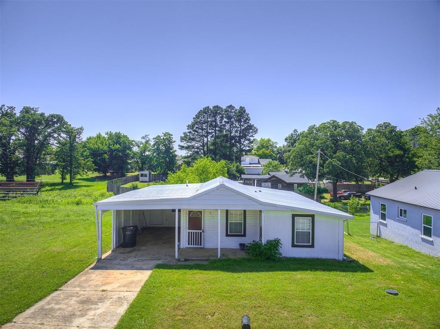 View of front of home with concrete driveway, a front yard, a carport, and view of scattered trees