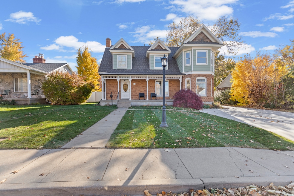 View of front facade featuring a porch, a front lawn, brick siding, and a chimney