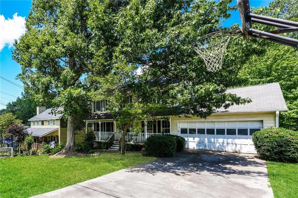 View of property hidden behind natural elements with asphalt driveway, covered porch, a garage, and a front yard
