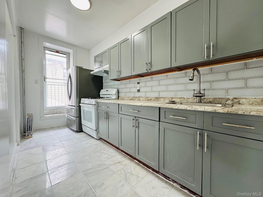 Kitchen featuring gray cabinets, decorative backsplash, gas range gas stove, and light stone counters