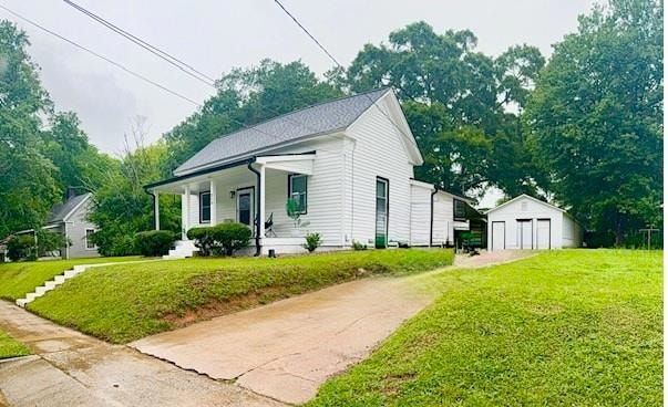 View of front of property featuring a porch, an outbuilding, driveway, a front lawn, and a detached garage