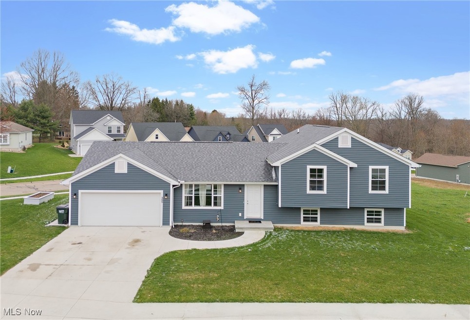 Split level home with concrete driveway, a residential view, an attached garage, a front yard, and a shingled roof