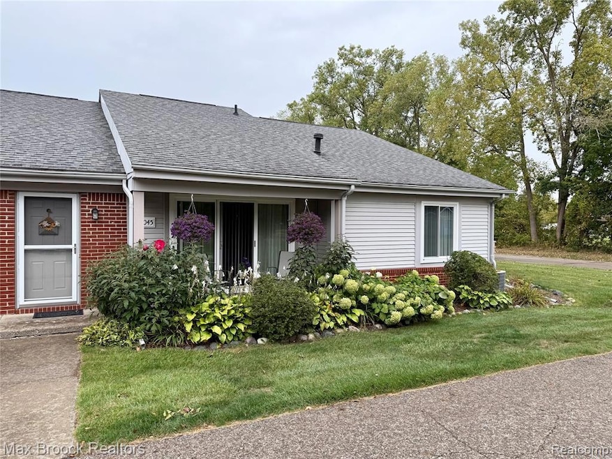 View of front facade featuring a front yard, a shingled roof, brick siding, and covered porch