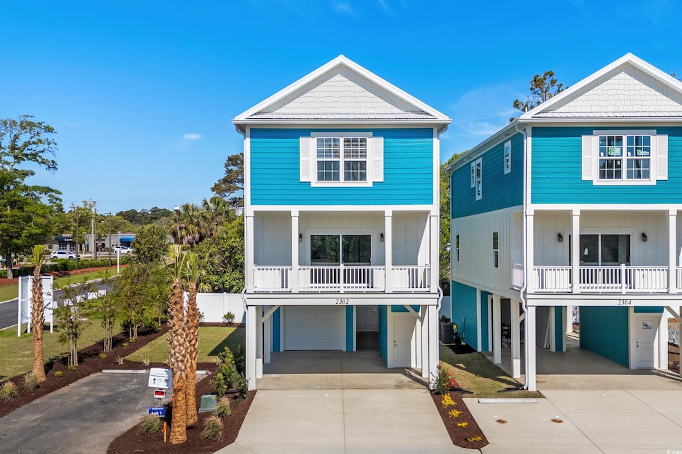 Raised beach house with concrete driveway, a carport, a balcony, board and batten siding, and an attached garage