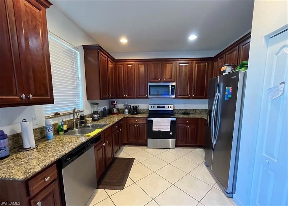 Kitchen with appliances with stainless steel finishes, light stone countertops, sink, and light tile patterned floors