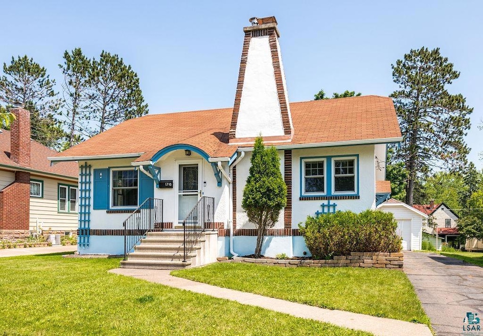 View of front facade with a chimney, a front yard, stucco siding, and roof with shingles