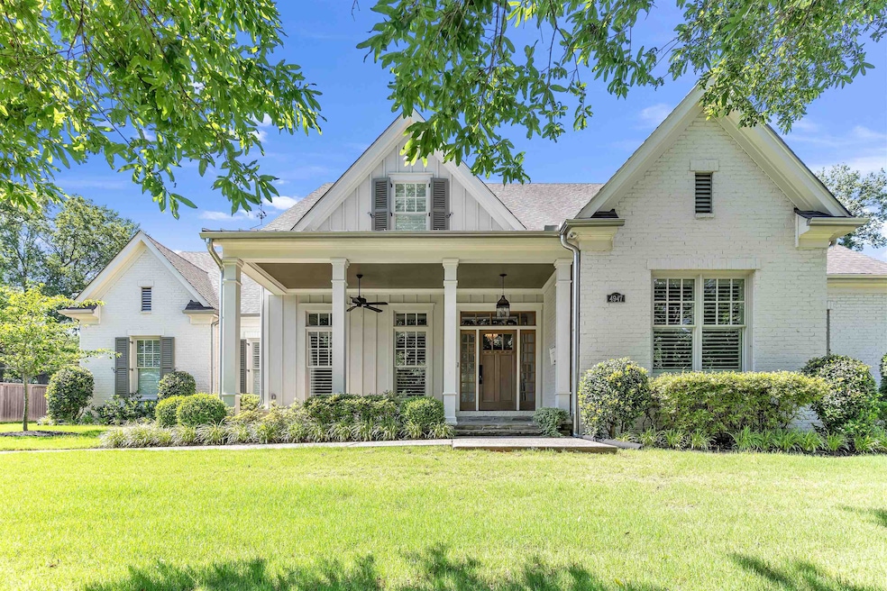 View of front of property with board and batten siding, ceiling fan, a front lawn, and brick siding