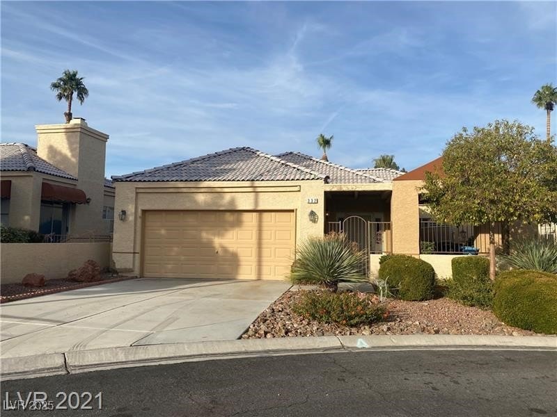 View of front facade with a tile roof, concrete driveway, stucco siding, fence, and an attached garage