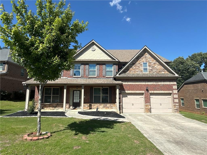 View of front of home with driveway, a front lawn, stone siding, and covered porch
