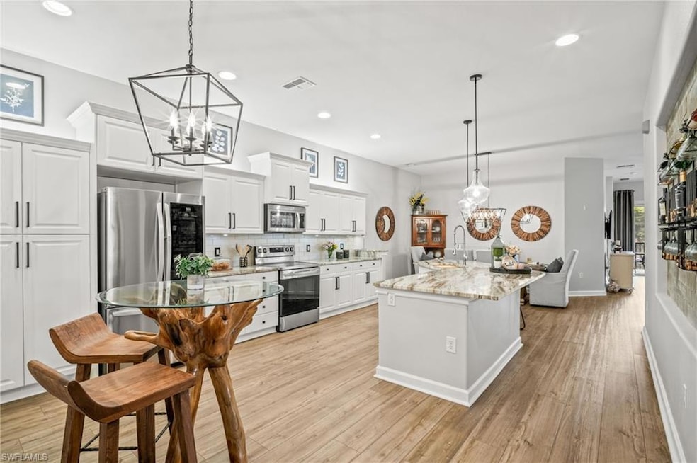 Kitchen with stainless steel appliances, a chandelier, light wood-style floors, backsplash, and recessed lighting