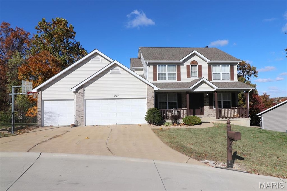 View of front facade with covered porch, driveway, a front yard, brick siding, and a garage