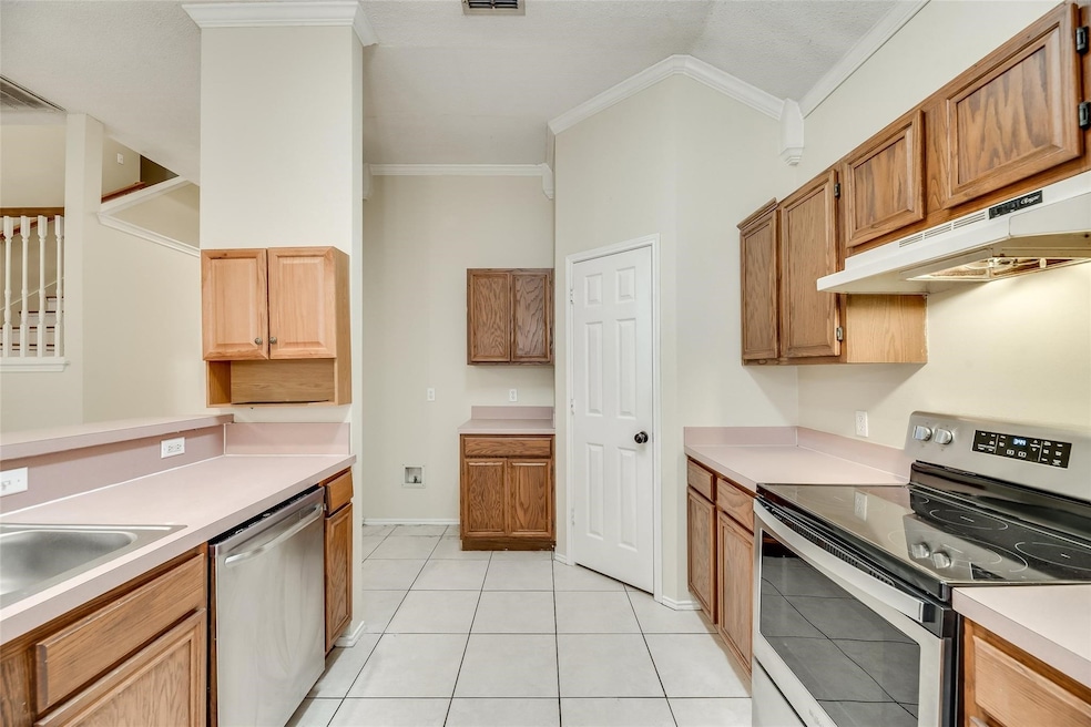 Kitchen with appliances with stainless steel finishes, ornamental molding, light countertops, under cabinet range hood, and light tile patterned floors
