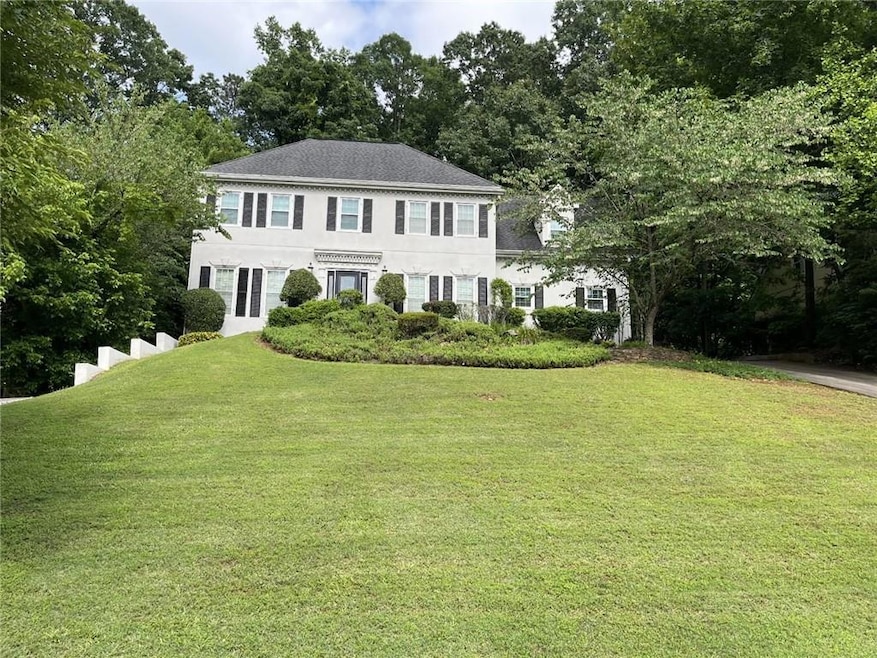 Colonial home with a front yard, stucco siding, and view of wooded area