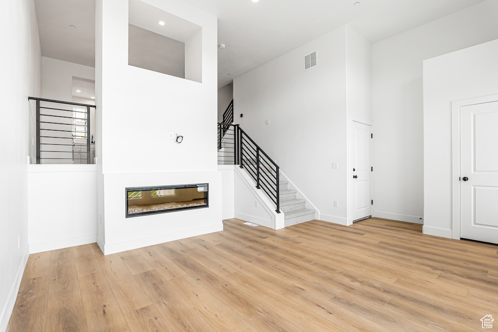 Unfurnished living room featuring stairway, light wood-style floors, a glass covered fireplace, and recessed lighting