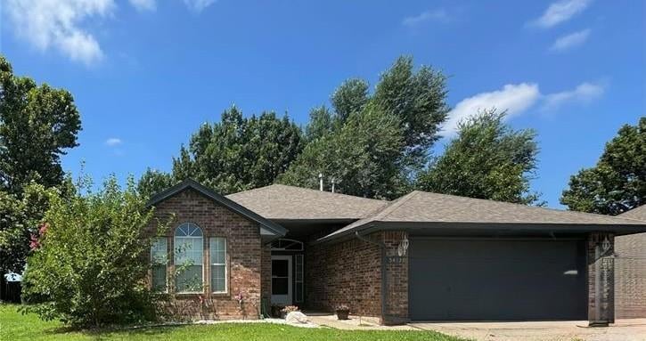 Single story home featuring brick siding, an attached garage, concrete driveway, a front yard, and roof with shingles
