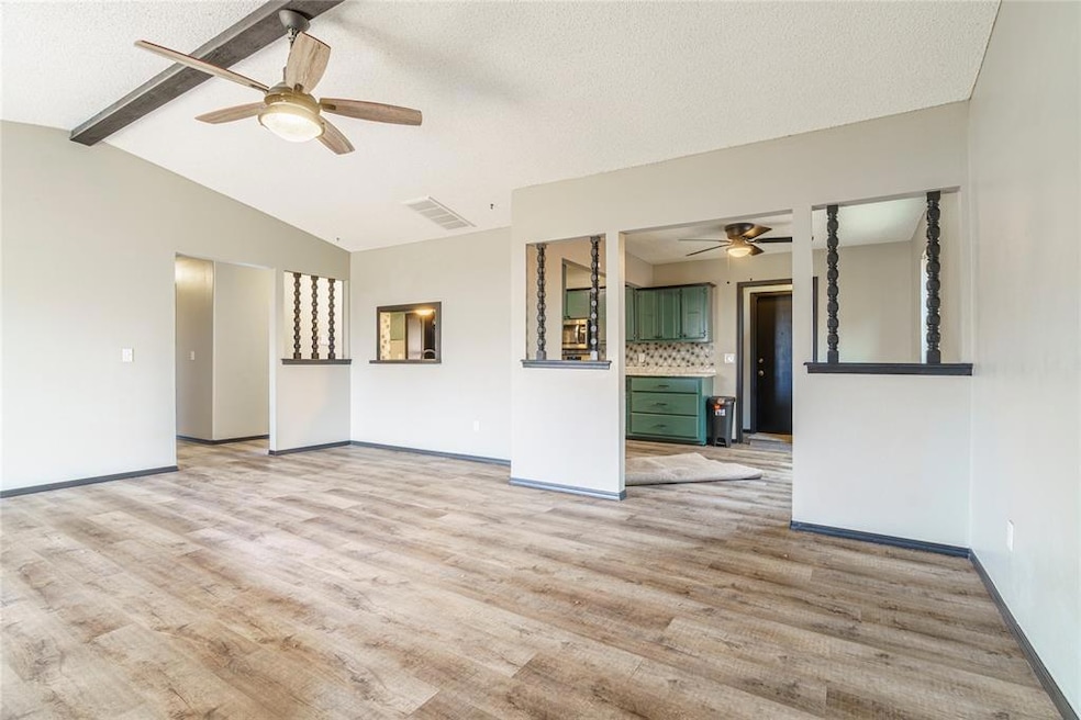 Empty room featuring lofted ceiling with beams, light hardwood / wood-style floors, and ceiling fan