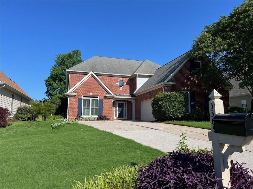 Traditional-style home featuring brick siding, a garage, a front lawn, concrete driveway, and a shingled roof