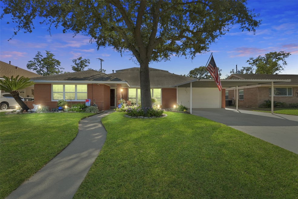 A charming single-story brick home with a well-maintained front yard, featuring a curved walkway and mature tree. The property includes a covered carport and is warmly lit, creating an inviting atmosphere.