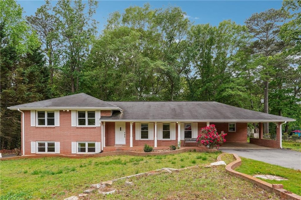 Split level home featuring a porch, brick siding, a carport, a front lawn, and concrete driveway