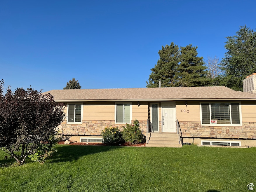 View of front of property with entry steps, stone siding, a front yard, and roof with shingles