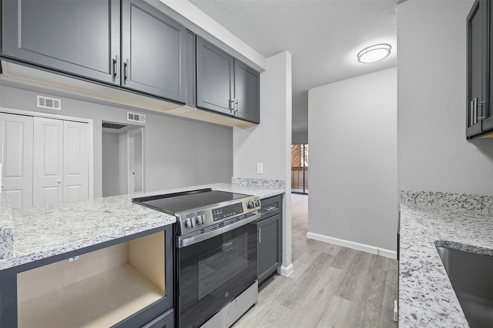 Kitchen with stainless steel electric range, light stone countertops, light wood finished floors, gray cabinets, and a textured ceiling