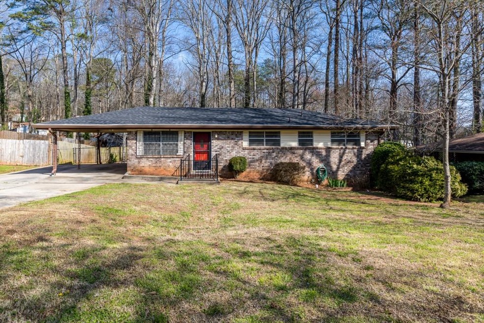 All brick ranch with covered parking on tree-lined