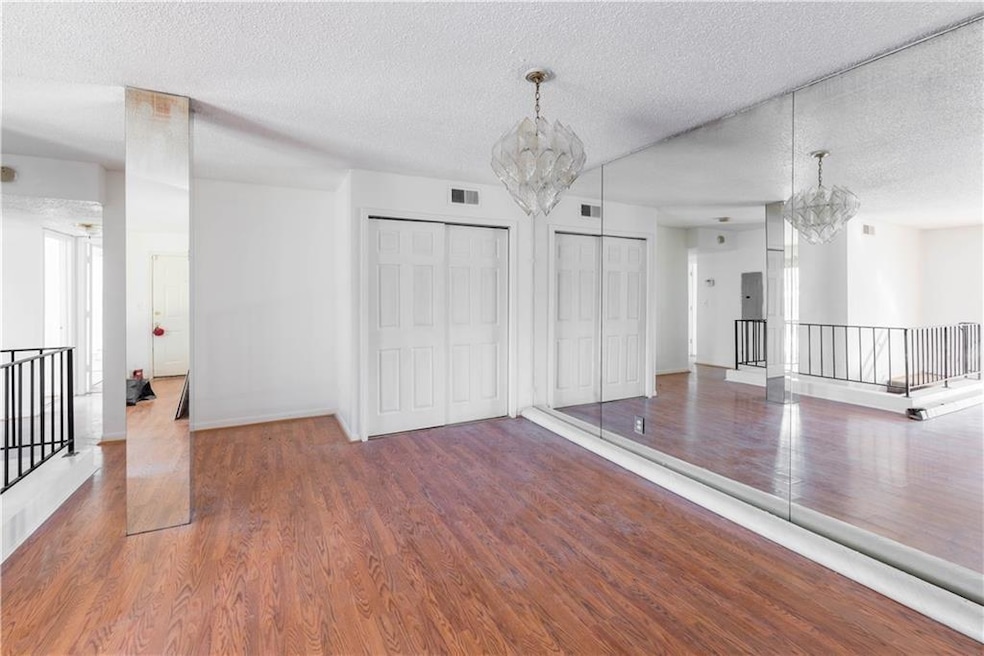 Unfurnished living room with a chandelier, wood finished floors, a textured ceiling, and baseboards