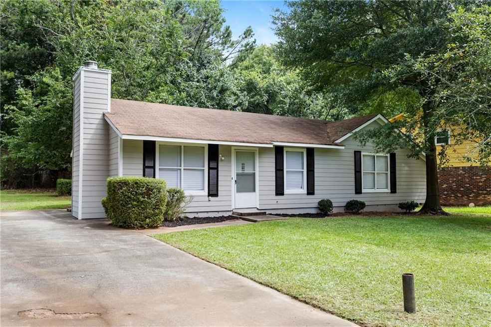 Ranch-style house with a front yard, a chimney, a shingled roof, and driveway