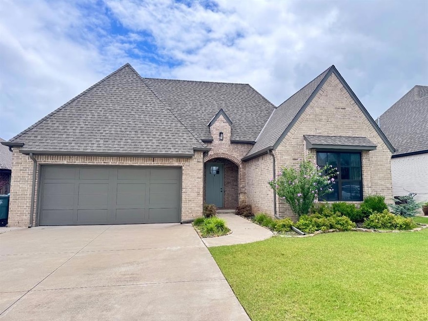 French country inspired facade featuring roof with shingles, brick siding, and concrete driveway