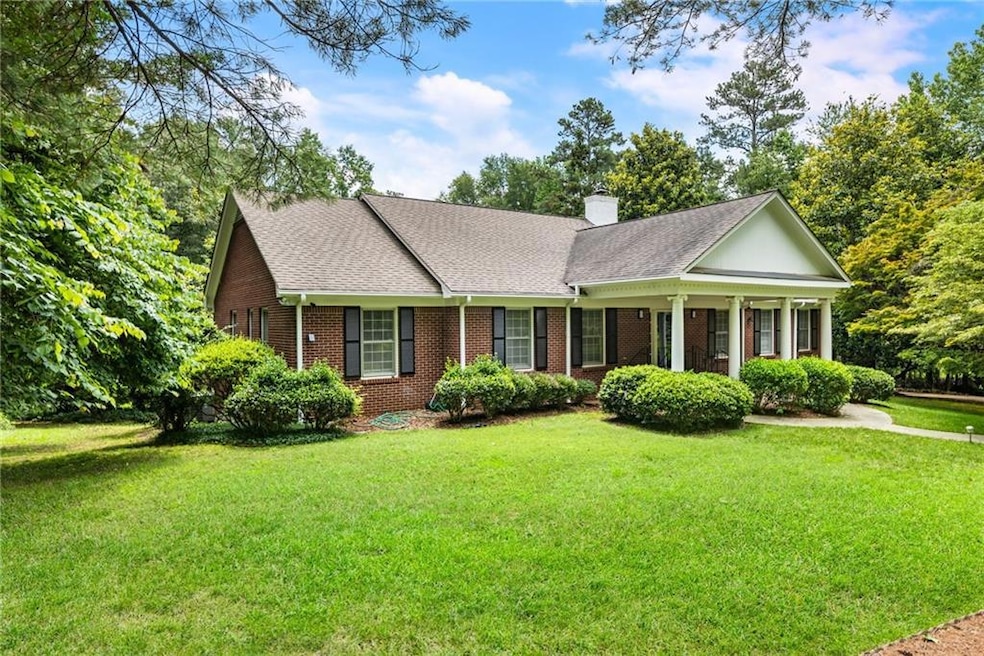 View of front of home with a front yard, brick siding, a chimney, and roof with shingles