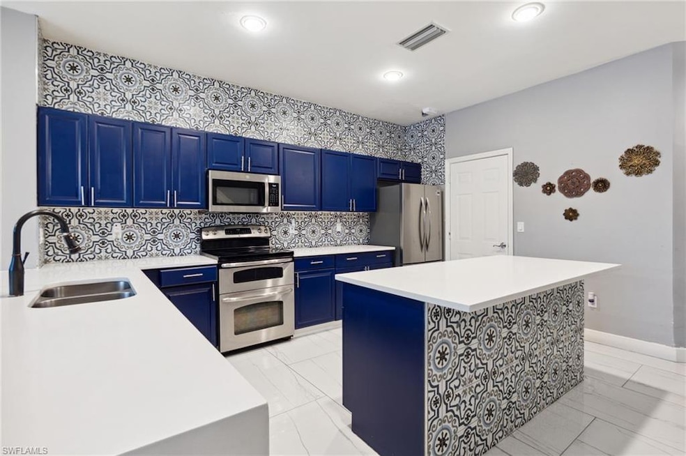 Kitchen featuring appliances with stainless steel finishes, a sink, blue cabinets, light marble finish floors, and recessed lighting