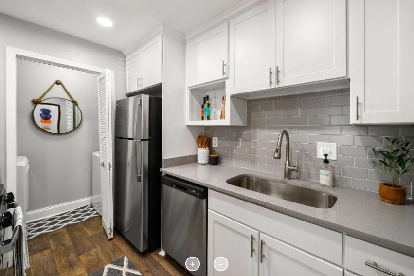 Kitchen featuring dark hardwood / wood-style flooring, appliances with stainless steel finishes, white cabinets, backsplash, and sink