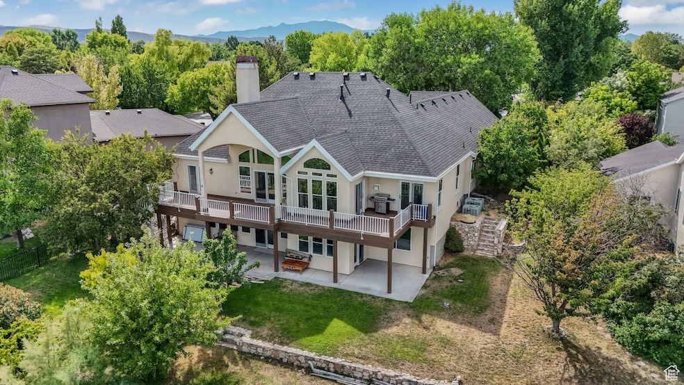Rear view of house featuring a patio, a chimney, stucco siding, a wooden deck, and a lawn